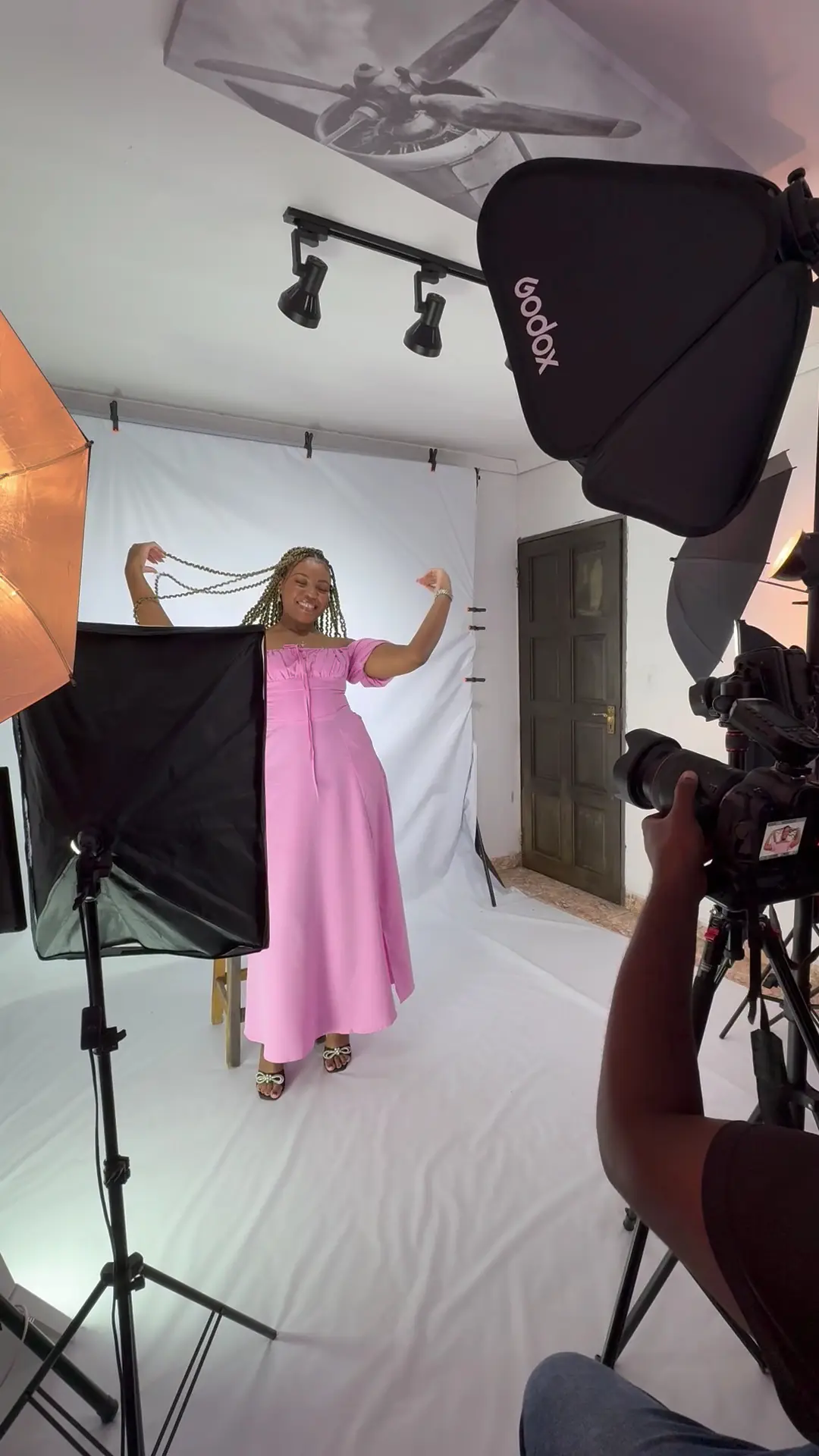 Behind the scenes in the studio: lights, a white backdrop and a pink dress