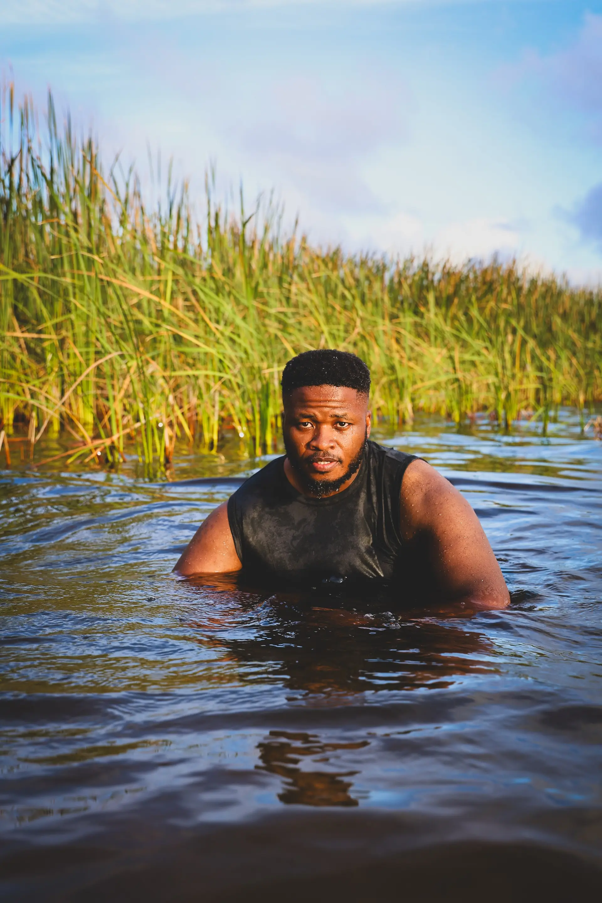 A man waist-deep in a river, reeds behind him